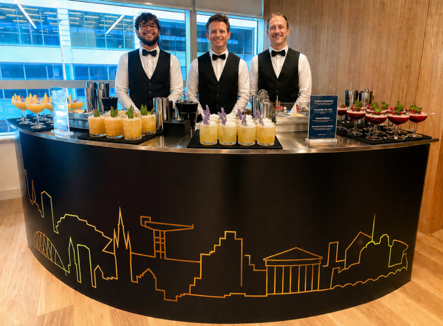 Bar Excellence pop-up bar with Glasgow skyline silhouette in gold, three bartenders preparing signature cocktails