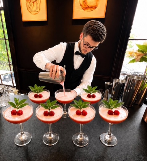 A Bar Excellence mixologist pouring a raspberry coupe cocktail for a row of guests at a live event bar