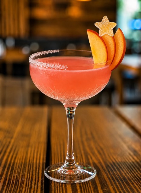 Peach and Ginger Margarita: a coral-pink cocktail in a coupe glass with a sugar rim, garnished with a fan of peach slices and a sugared ginger star
